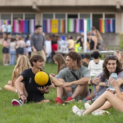 学生们坐在展示多面旗帜的大楼前的草地上聊天.